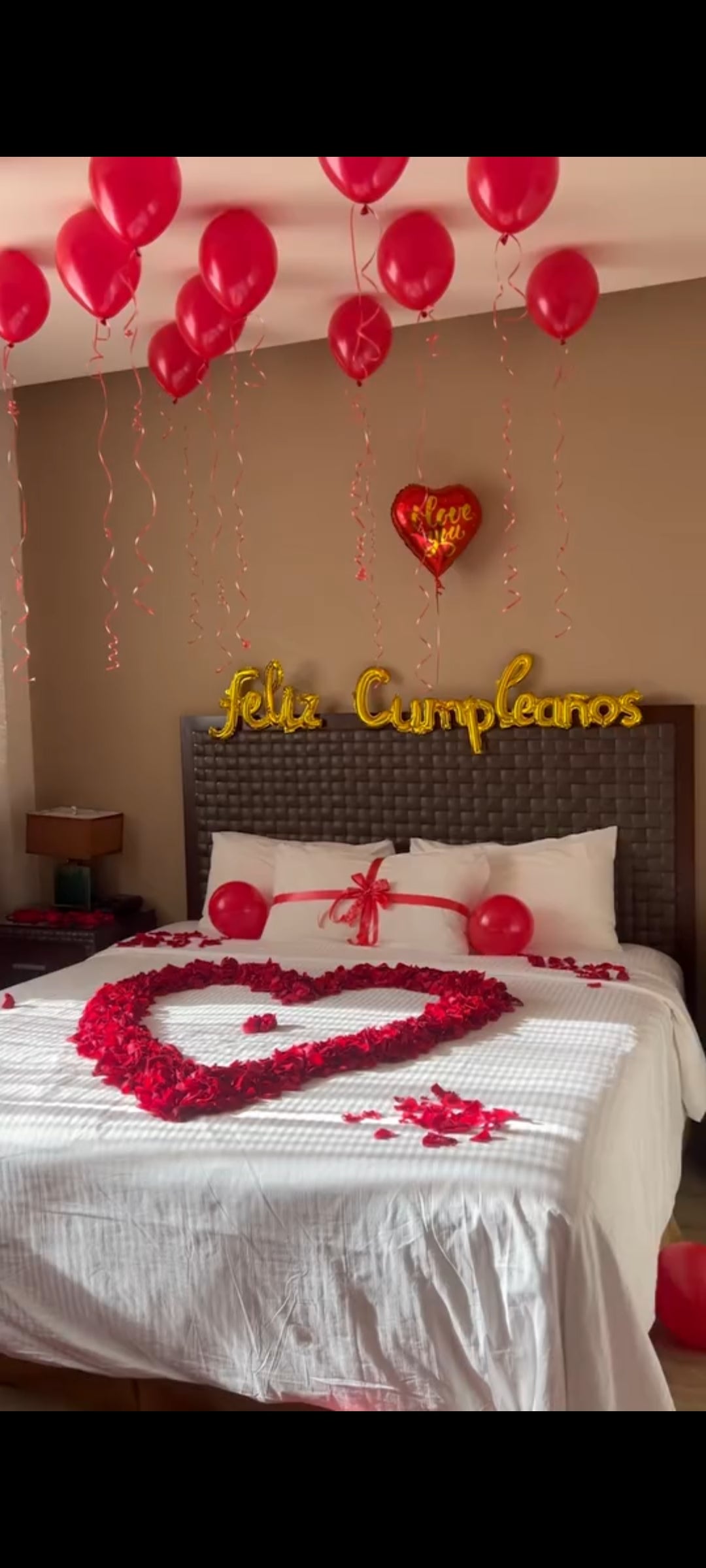Decoración romántica de habitación con globos rojos, pétalos de rosa en forma de corazón y letras Feliz Cumpleaños